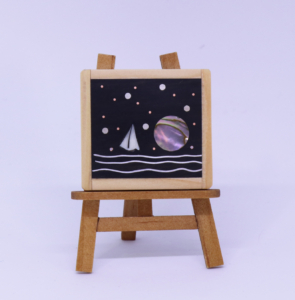 Miniature picture of sailboat and moon made out of recycled materials (beer can, piano keys, hemlock, copper)