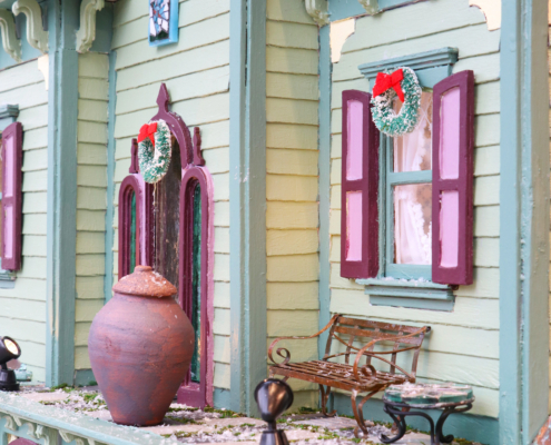 Miniature scene of the deck outside of the victorian, pot, bench, glass table, hanging mosaic and snow.